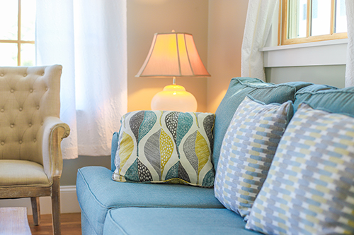 Seating area with a blue couch, beige chair, and lamp beneath a window